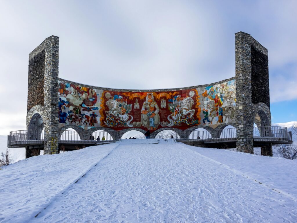 Low angle of old stone arched Russia Georgia Friendship Monument with tile mural inside located on snowy hill in Gudauri